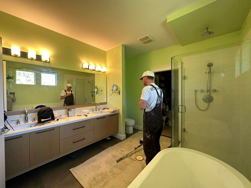 Painter working in modern bathroom with light green walls and glass shower
