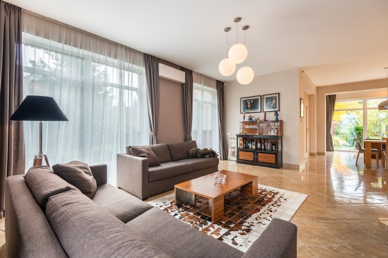Modern living room with neutral sofas, wooden coffee table, soft lighting, large windows, and an open layout showcasing practical and stylish interior designing.
