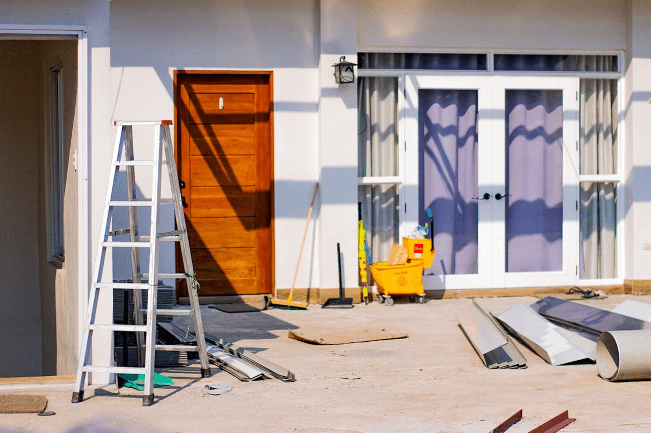 Exterior home repair scene with ladder, tools, and renovation materials set outside a house, showing ongoing home repair work that may require professional assistance.