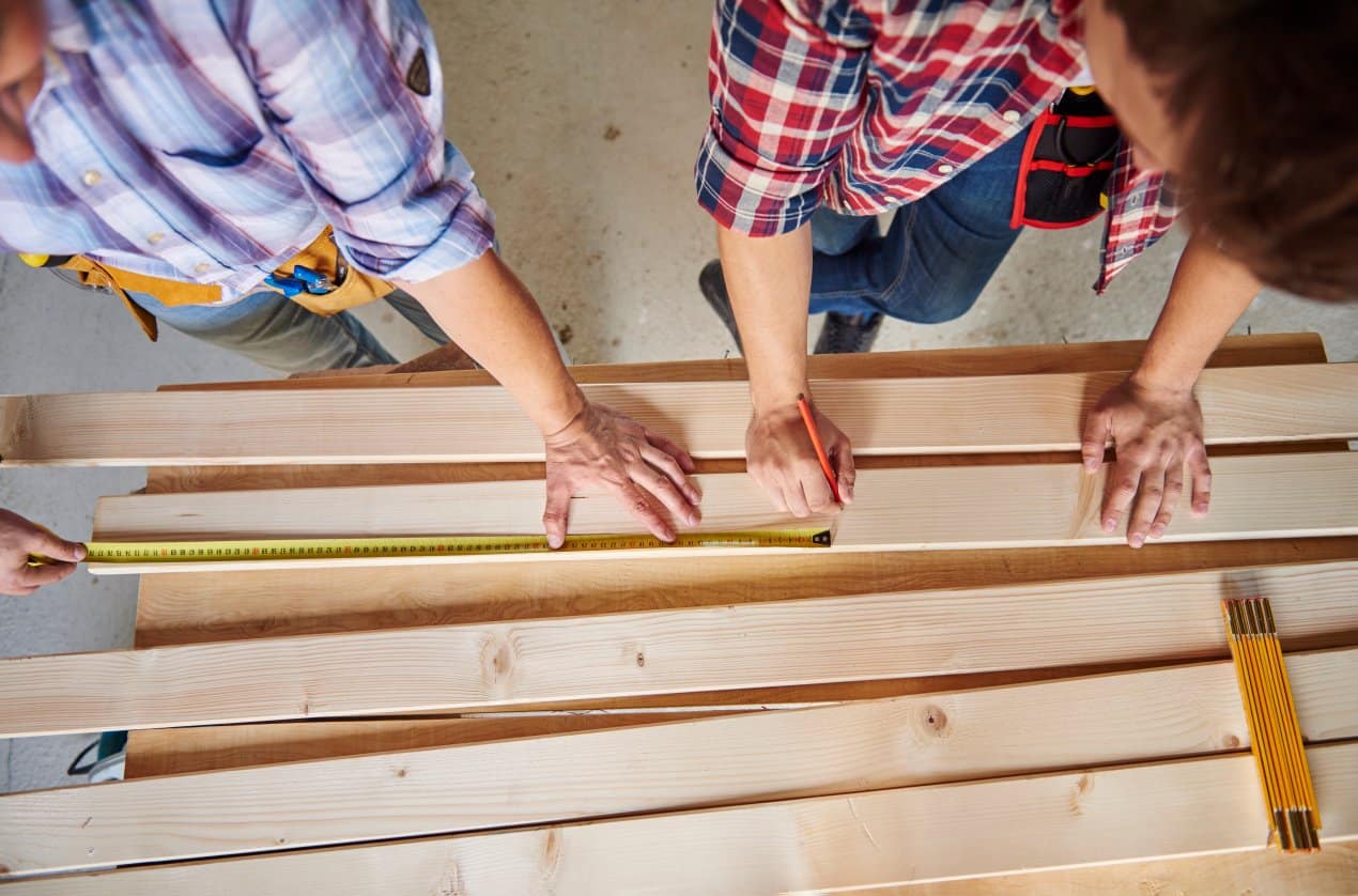 Workers measuring and marking wooden boards during fence panel preparation at a Decking Manufacturer production workshop.