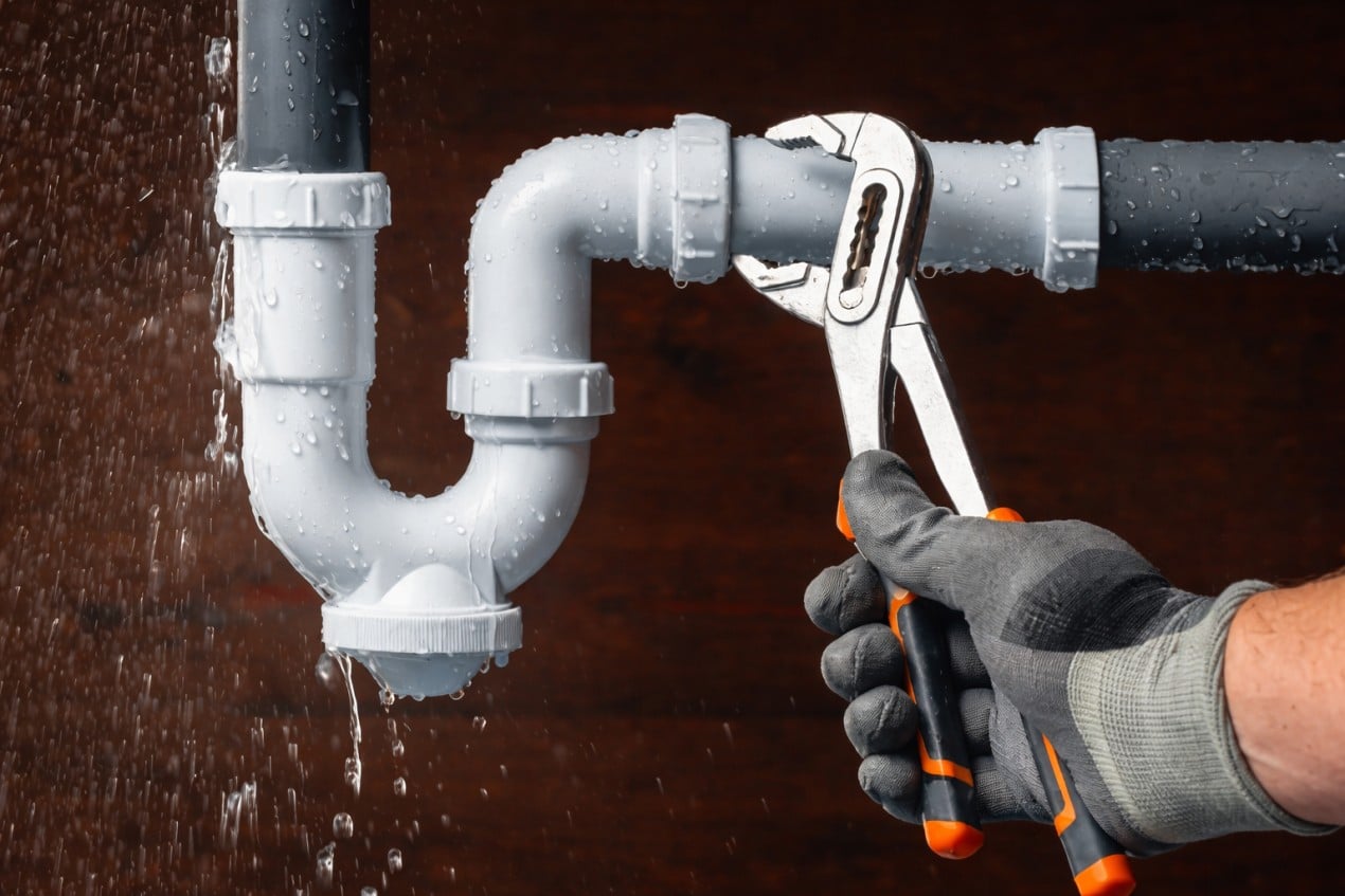 Local Plumber tightening leaking PVC pipe under sink, water dripping, emergency plumbing repair in home kitchen setting