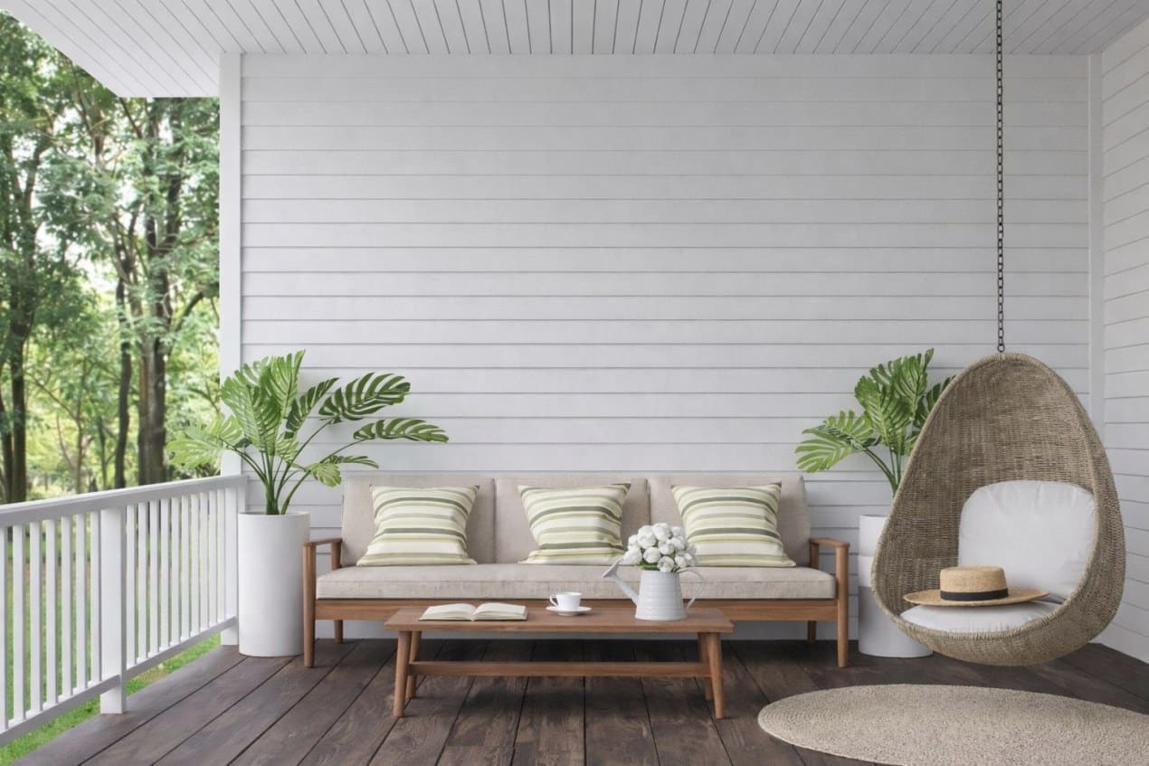 Cozy outdoor living space with sofa, cushions, wooden table, hanging chair, and plants blending indoor comfort with a covered patio design