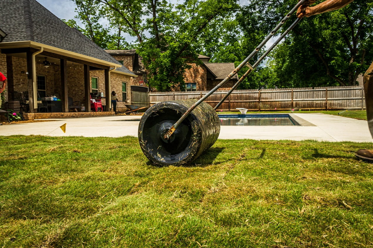 Professional Lawn Maintenance worker rolling and caring for grass in a backyard near a home patio and swimming pool.