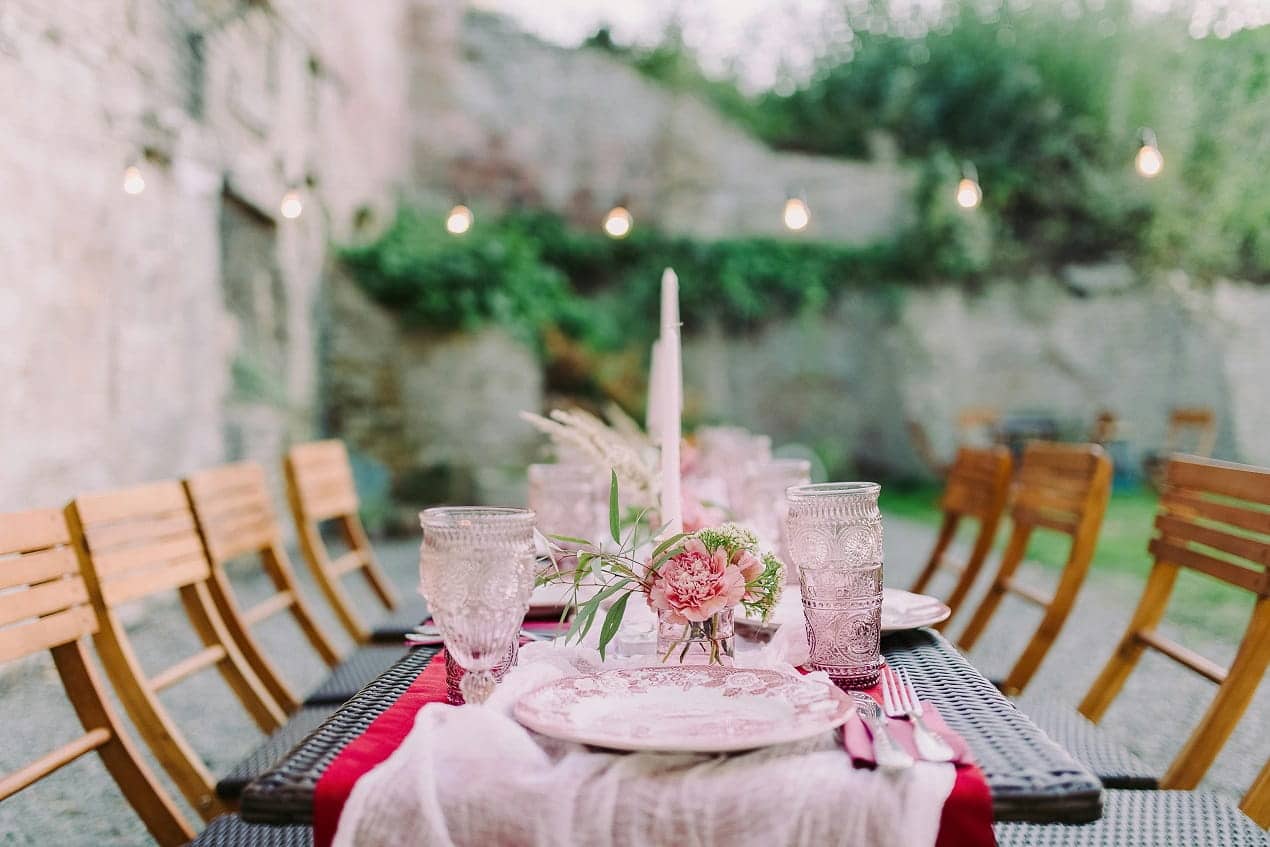 Outdoor table setup for Backyard Graduation Parties with chairs, plates, glasses, flowers, and string lights in a garden.