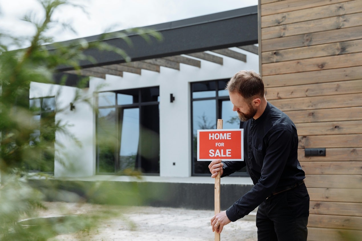 Man placing home for sale sign outside modern house, representing smart home buying, property search, and confident real estate decision making