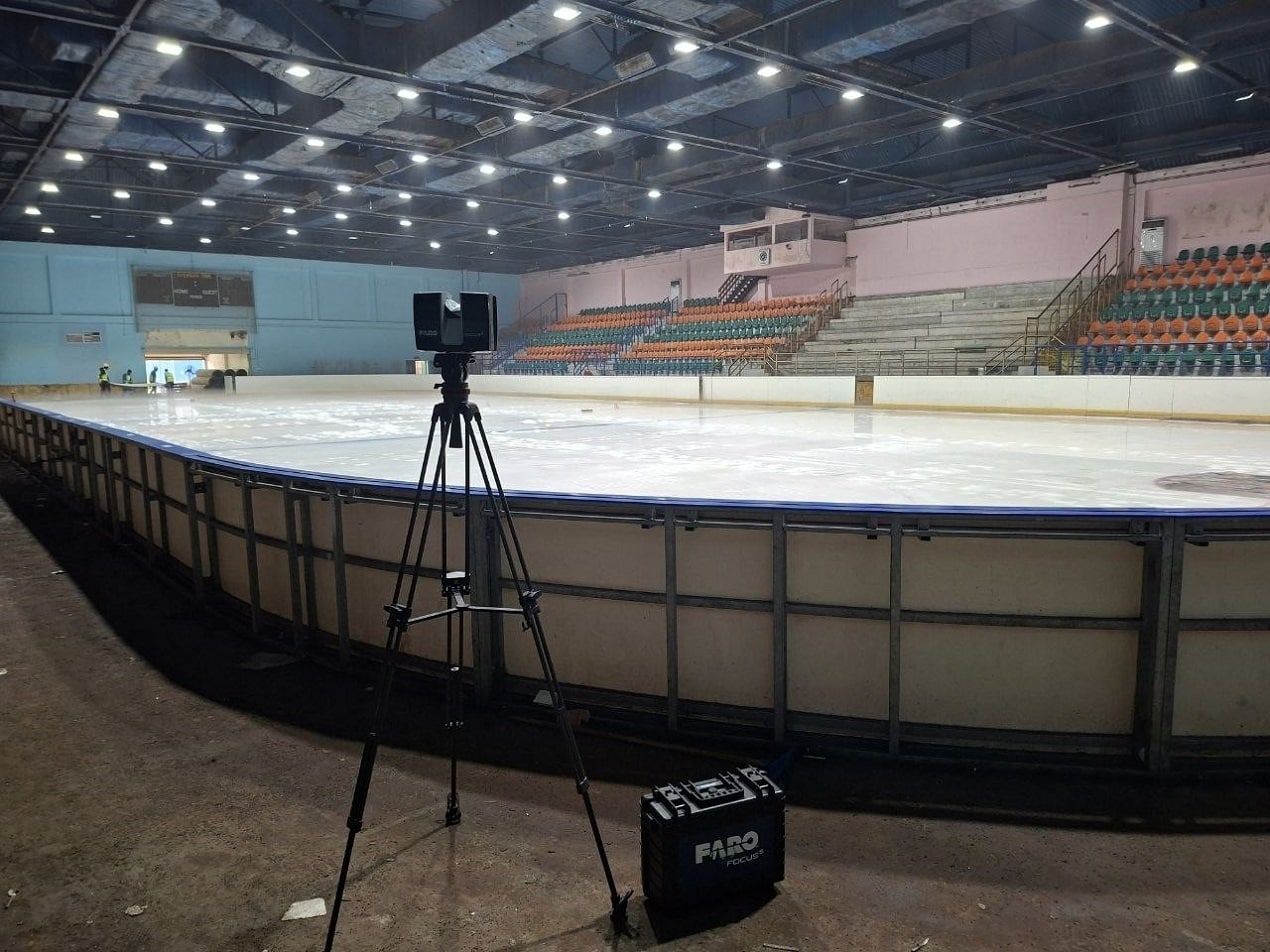 Laser Scanning equipment set on a tripod inside an indoor ice arena to capture accurate measurements of the rink and seating area.
