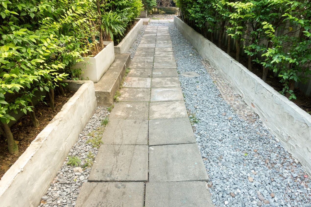 Natural Stone Tiles used on an outdoor garden walkway with gravel borders, greenery, and low retaining walls.