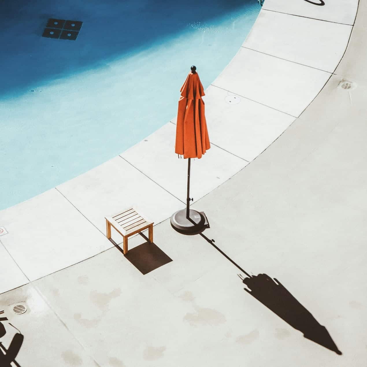 Closed patio umbrella and side table as poolside pool accessories beside outdoor swimming pool
