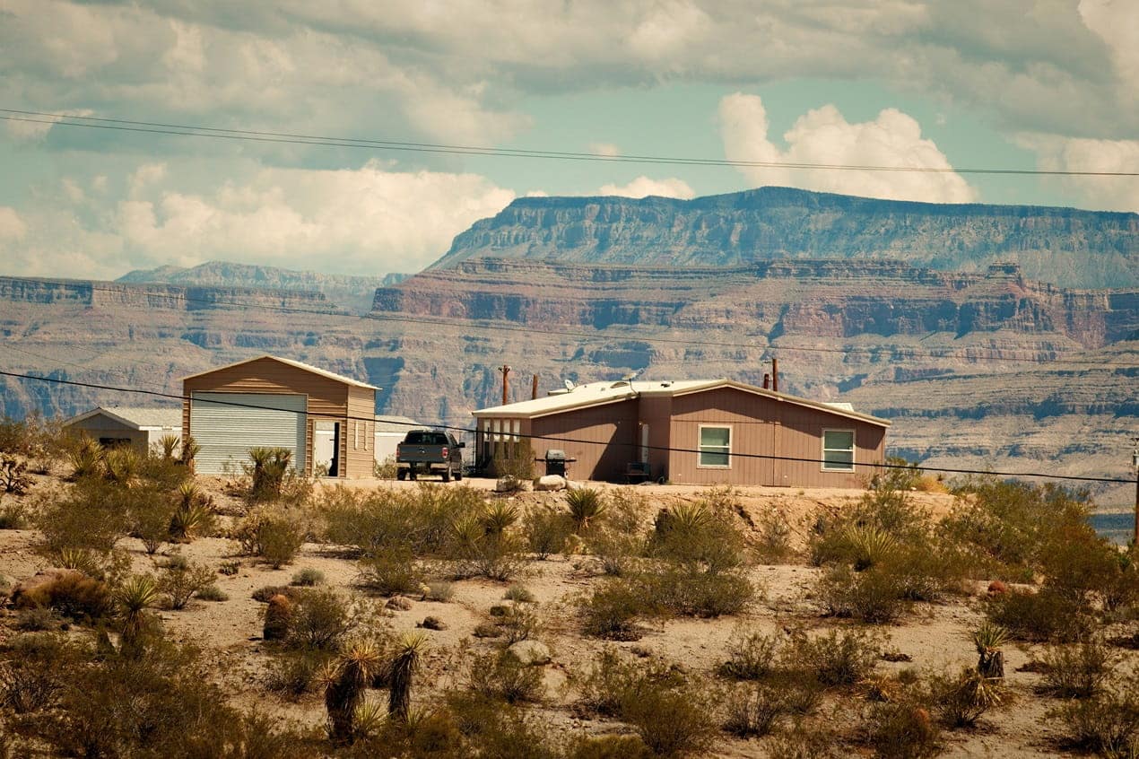Desert home in a hot, dry landscape with windows exposed to intense sunlight, illustrating ways to reduce desert home cooling costs.
