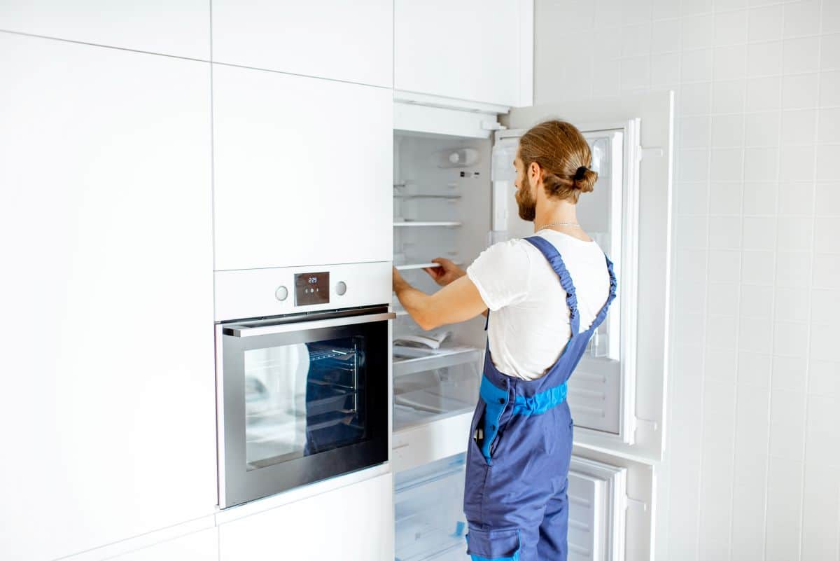 Technician inspecting the interior of a built-in luxury refrigerator in a modern white kitchen